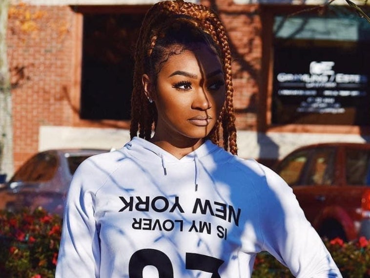 Woman with braids in a white hoodie on a sunny street.